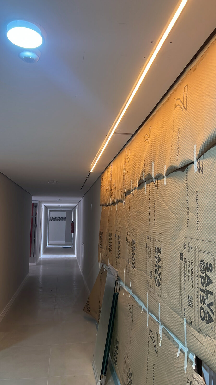 Corredor predial com iluminação linear em LED e revestimento em obra